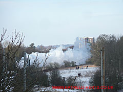 Cloud of steam from Tornado with the top of Goldings House - a Sixties tower block - visible in the background and people in the fields