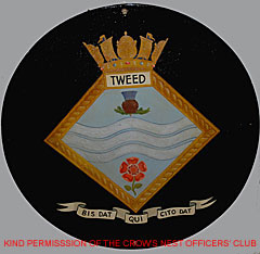 HMS Tweed's gunshield with ship's crest - gold bordered diamond against a circular black field. The diamond area has a crown on top of it and the name Tweed below. Within the diamond at the top is a thistle and a rose at the bottom corners, with three wavy lines through the middle. Motto scroll at the base reads Bis Dat Qui Cito Dat